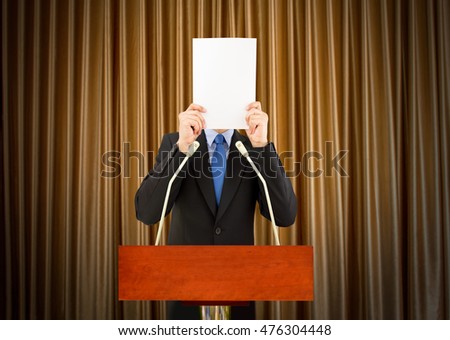 businessman with stage fright covering his face with a sheet of paper to a podium to speak for being embarrassing