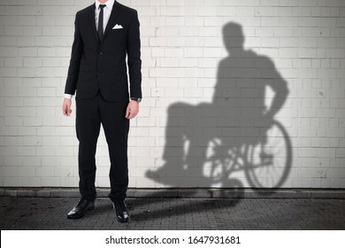 Businessman Standing Against White Brick Wall With Shadow Of A Disable Man Sitting On Wheelchair