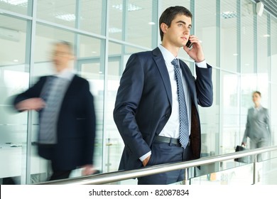 Businessman standing by banisters and calling with walking people on background - Powered by Shutterstock