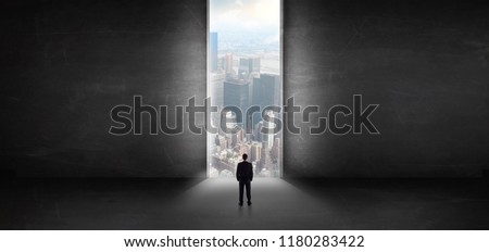 Businessman standing in a dark room and looking outside to a cityscape view