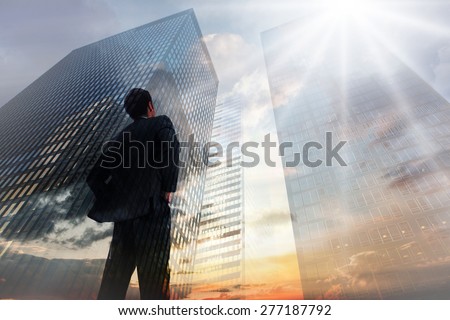 Businessman standing with hands on hips against low angle view of skyscrapers at sunset
