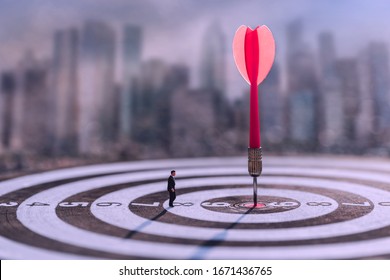 Businessman standing lookup red dart arrow hitting target centre dartboard on blurred cityscape background. Business targeting and focus.