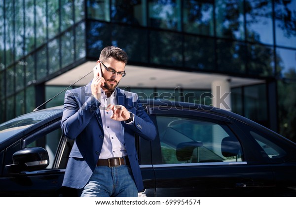 Businessman standing near the car. Office\
building on the\
background