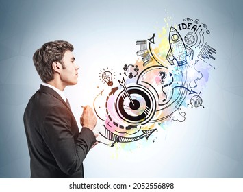 Businessman is standing near sketch with icons of rocket launch, start up, light bulb, globe, bar and pie diagrams, teamwork, plan and arrow. Concept of inspiration and imagination for creative idea