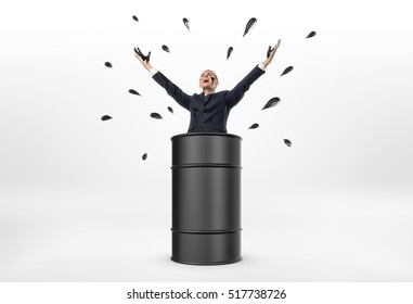 A Businessman Standing In An Oil Barrel With His Arms Up And Oil Drops Around Him On The White Background. Oil And Petroleum Products. Black Gold. Resource Extraction.