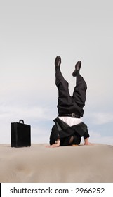 Businessman standing on his head with his head in the sand