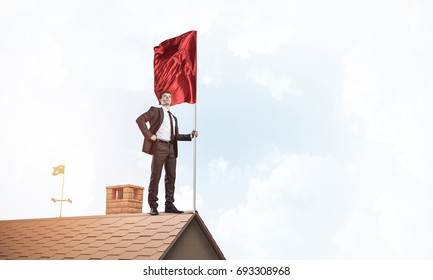Businessman standing on house roof and holding red flag. Mixed media - Shutterstock ID 693308968