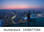 Businessman standing on open roof top balcony watching city night view . Business ambition and vision concept .