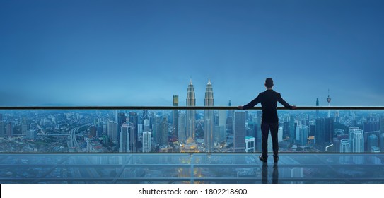 Businessman standing on open roof top balcony watching city night view . Business ambition and vision concept . - Shutterstock ID 1802218600