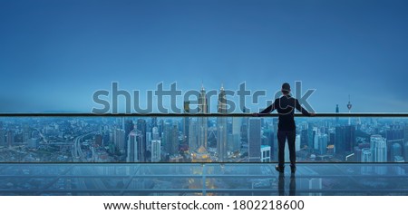 Businessman standing on open roof top balcony watching city night view . Business ambition and vision concept .