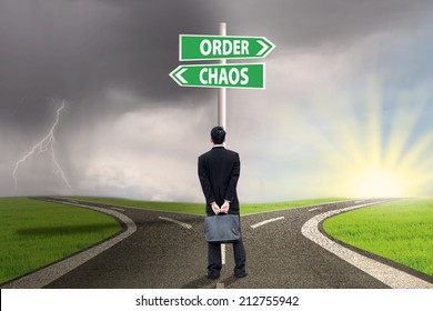 Businessman standing on the road looking at signpost of order and chaos