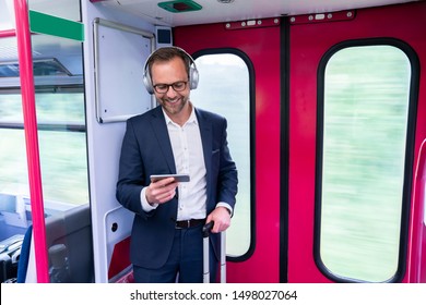 Businessman Standing On Train Streaming Movie From Mobile Phone To Wireless Headphones