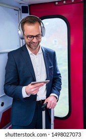 Businessman Standing On Train Streaming Movie From Mobile Phone To Wireless Headphones