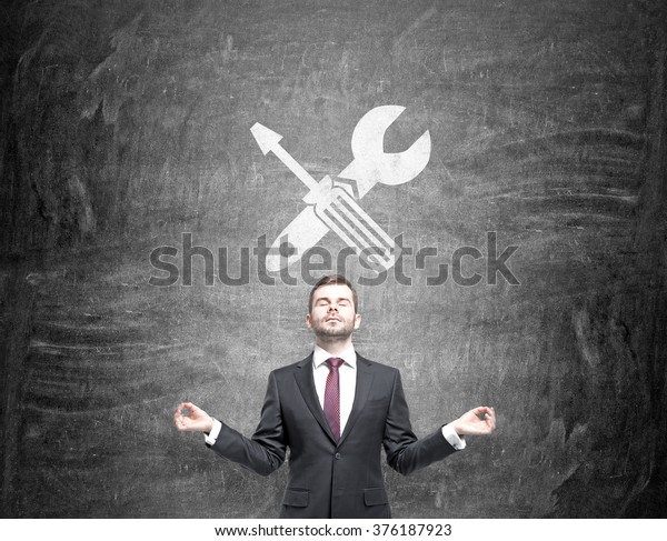 A businessman standing in\
the posture of meditation, a screwdriver and a wrench crossed are\
drawn on a blackboard over his head. Front view. Concept of fixing\
things.