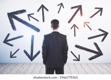 Businessman standing puzzled in front of a wall with multiple black arrows pointed in different directions, decision making and career path concept - Powered by Shutterstock