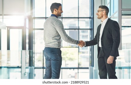 Businessman standing, smiling and with a handshake, greets a colleague in an office. Executive meets client or partner and shakes hands. Two happy professionals agree on a successful business - Shutterstock ID 2188929521