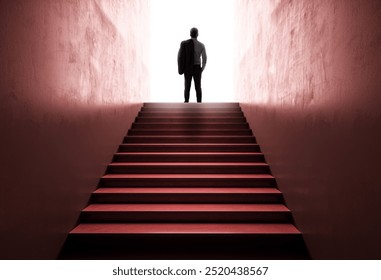 Businessman standing at the top of a staircase, silhouetted against a bright light, symbolizing success and ambition on a dark background. Concept of career growth and vision - Powered by Shutterstock