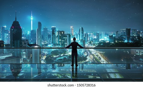 Businessman standing at transparent glass floor on rooftop with night city panoramic view.