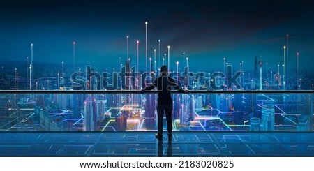 Businessman standing at transparent glass floor on rooftop with night Smart city panoramic view. Business success with smart technology concept