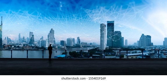 Businessman Standing Using Smart Phone In Modern Space Watching City Night View.Business Wireless Network And Connection Technology Concept.