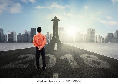 Businessman Standing While Looking At Upward Arrow On The Road With Number 2018, Symbolizing Of Better Career In The Future