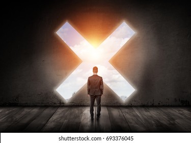 A businessman stands with his turned back and looks into a cross-shaped hole in a concrete wall. Time to stop. Avoid business pitfalls. Trouble ahead.
