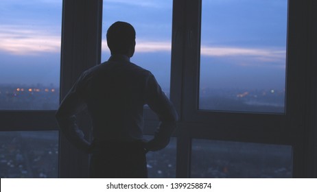 Businessman stands near the window and looks on night city background. - Shutterstock ID 1399258874