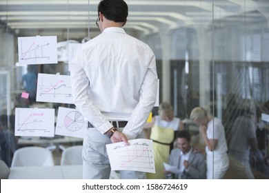 Businessman Studying Documents Stuck To Glass Office Wall