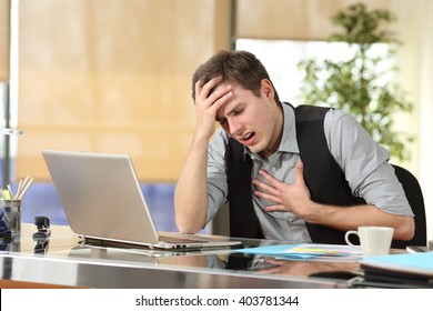 Businessman suffering an anxiety attack with the hands in his chest and head sitting in a desktop at office