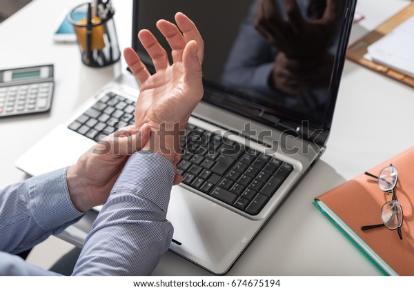 Businessman suffering\
from wrist pain in\
office