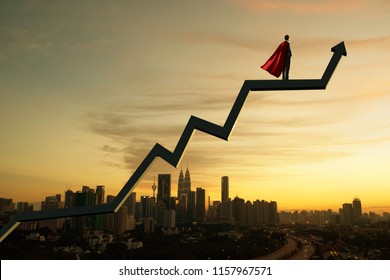 Businessman In Suit And Cape Hero And Charts With Sunrise City Skyline Background . Financial Economic Growth Concept