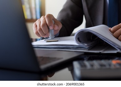 Businessman in suit hand stamping rubber stamp on document in folder with laptop computer on the desk at office. Authorized allowance permission approval concept.