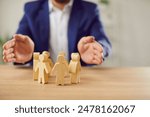 Businessman in suit holding hands above wooden toy people figures standing in circle at desk protecting human rights. Society, people community care and safety concept in business.