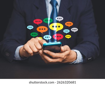 Businessman in suit holding smartphone with vibrant chat icons emerging from the screen, symbolizing online messaging, communication apps, and digital networking in modern business.