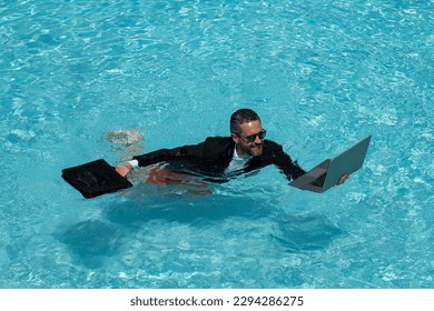 Businessman in suit with laptop in swimming pool. Crazy business man on summer vacation. Excited businessman in wet suit in swim pool. Funny business man, crazy comic business concept. Remote working.