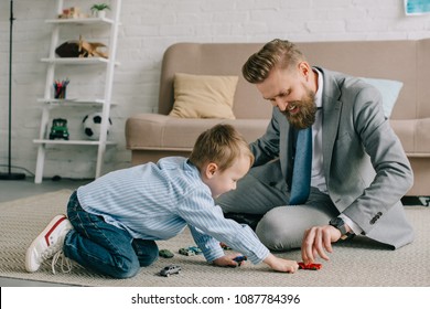 businessman in suit and little son playing with toy cars on floor at home, work and life balance concept