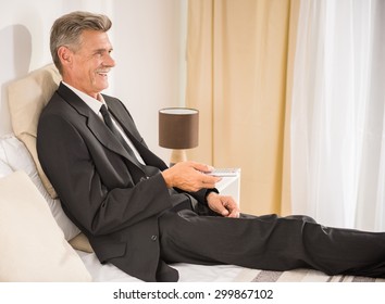 Businessman In Suit Lying On Bed And Watching TV At The Hotel Room. Side View.