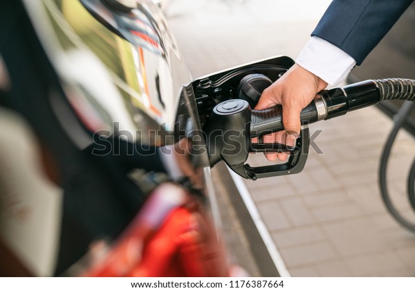 A
businessman in a suit manages his car with gasoline at a gas
station. Hand and black refueling gun
close-up.