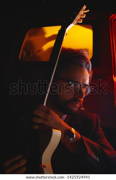 Businessman in a suit playing an electric guitar\
at night in the red light near the\
car