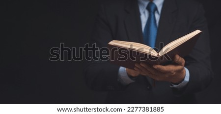Businessman in a suit reading a book while standing on a black background. Space for text. Education and reading a book concept