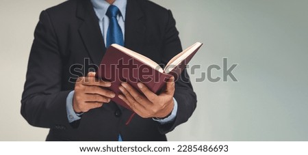 Businessman in a suit reading a book while standing against a gray background. Space for text. Education and reading a book concept