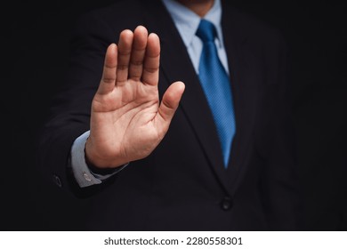A businessman in a suit shows a stop gesture while standing on a black background. Space for text. Close-up photo - Shutterstock ID 2280558301