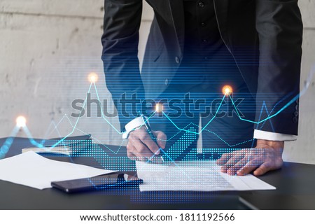 Businessman in suit signs contract. Double exposure with financial chart hologram. Man signing mortgage agreement. Real estate market analysis and investment concept.