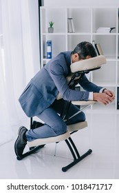 businessman in suit sitting in massage chair at office