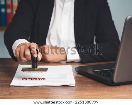 Businessman in a suit stamped for canceled documents while sitting at the table in the office. Business and document management concept