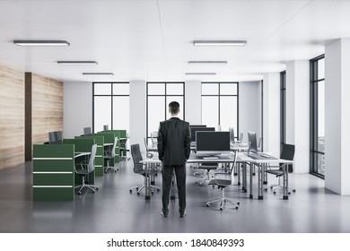 Businessman In Suit Standing In Office Interior With Computers On Green Table. Workplace And Lifestyle Concept.