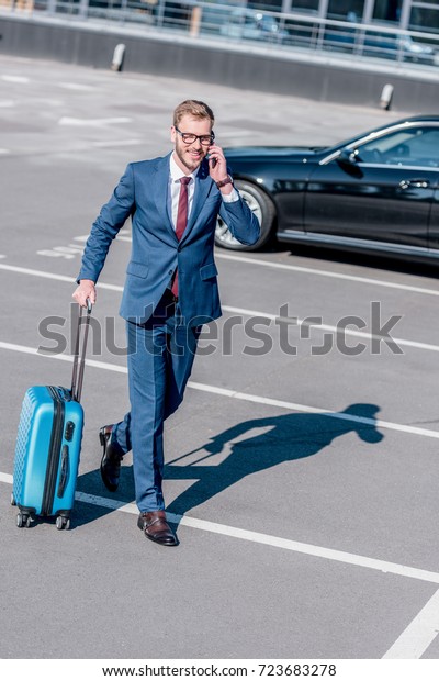 businessman in suit with suitcase for business\
trip using\
smartphone