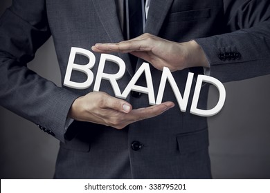 Businessman in suit with two hands in position to protect the word "BRAND" (focus on hand, blur out the suit).
