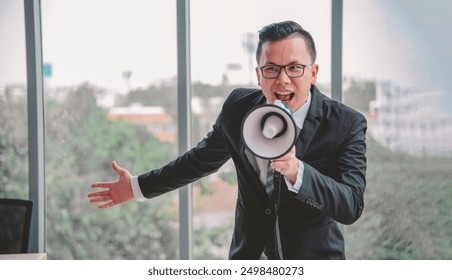 Businessman in suit using a megaphone to emphasize an important announcement in a modern office environment with large windows and outdoor view. - Powered by Shutterstock