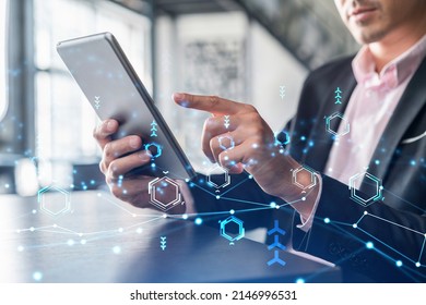 Businessman in suit using tablet device to optimize development by implying new technologies in business process. Interconnections and hi tech hologram over modern panoramic office background